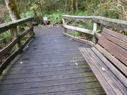 End of wetland boardwalk with railing connects to gravel trail – transition may have high lip – directional sign – bench
